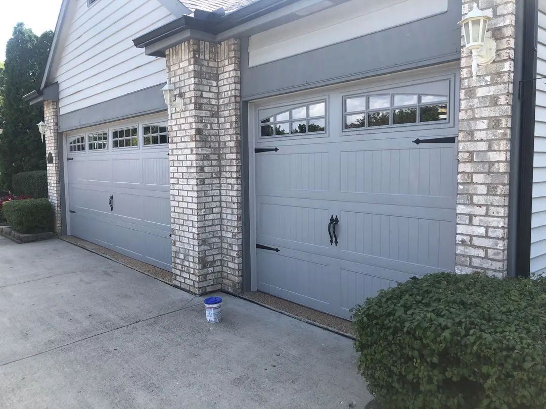 Gray carriage-style garage doors with windows and black hardware